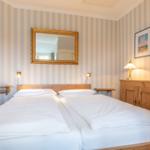 Two beds with white bedding, wooden furniture, and striped walls.