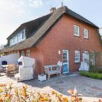 Red brick house with thatched roof and terrace with garden furniture.