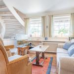 Living room with sofa, armchairs, TV, and staircase. Windows with curtains and rug.