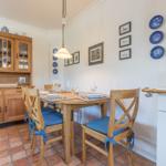 Dining room with wooden table, chairs, and kitchen area. Wall with pictures and blue plates.