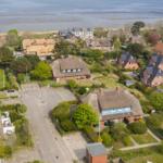 Village with thatched houses and green gardens by the water.