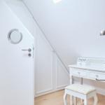 Schlafzimmer mit weißem Schrank, Schreibtisch und Stuhl unter schräger Decke.