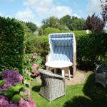 Garten mit Strandkorb, Tisch und Stühlen umgeben von Sträuchern und Blumen.