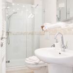 Bad mit Dusche, Waschbecken und Toilette. Steinverkleidung und Spiegel.