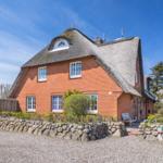 Red brick house with thatched roof and garden fence.