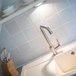 Kitchen faucet with cutting board and knives against gray tiled wall