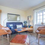 A living room with blue sofa, two brown leather chairs, and wooden floor.