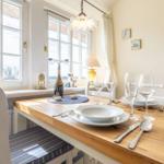 Dining room with wooden table, white chairs, and windows with view outside.