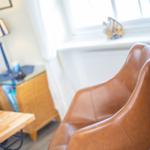 A brown leather sofa in front of a window with white curtains.