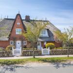Red brick house with thatched roof and white gate