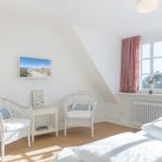 Schlafzimmer mit Dachschräge, zwei weißen Stühlen und Fenster mit rotem Vorhang.