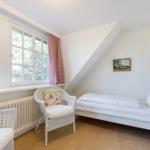 Ein Schlafzimmer mit Dachschrägen, Fenster, Bett und Stühlen.