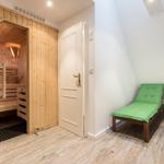 Sauna mit Glaswand und zwei grünen Liegen im Dachgeschoss.
