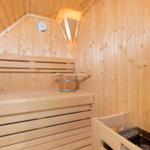 Sauna mit Holzbank, Thermometer und Eimer.