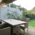 Terrasse mit Tisch und Stühlen, umgeben von Grün und weißem Zaun.