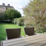 Terrasse mit Tisch und zwei Stühlen. Grünfläche und Bäume im Hintergrund.