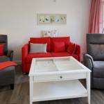 Ein Wohnzimmer mit rotem Sofa, zwei grauen Sesseln und einem weißen Couchtisch.