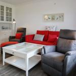 Ein Wohnzimmer mit rotem Sofa, grauen Sesseln und weißem Couchtisch.