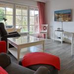Wohnzimmer mit Glas-Tisch, roten Kissen und TV an der Wand.