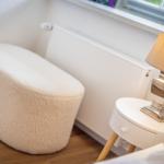 Weißer, flauschiger Sitzhocker neben Nachttisch mit Lampe.