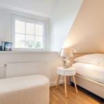 Schlafzimmer mit Bett, Nachttisch und Fenster. Bücher stehen auf der Fensterbank.