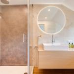 Dusche mit Glaswand, Waschbecken mit runden Spiegel und Holzunterschrank.