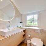 Badezimmer mit Waschtisch, Spiegel und Fenster. Toilette und Heizung sind vorhanden.