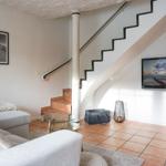 Wohnzimmer mit Sofa, Glas-Tisch und Treppenhaus. Fernseher an Wand montiert.