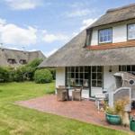 Haus mit Strohdach, Terrasse und Garten. Möblierte Außenterrasse mit Tisch und Stühlen.