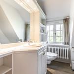 Badezimmer mit Waschbecken, Spiegel, Toilette und Fenster.