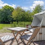 Terrasse mit Tisch, Stühlen und Strandkorb. Hintergrund: grüner Garten und Bäume.