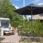 Terrasse mit Strandkorb, Sonnenschirm und Gartenhaus im Hintergrund.