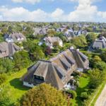 Dorf mit strohgedeckten Häusern und grünen Gärten unter blauem Himmel.
