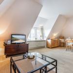 Wohn- und Essbereich mit Holzboden, TV, Tisch und Stühlen unter schrägen Dachdecken.