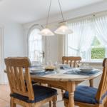Esszimmer mit Holztisch, Stühlen und Fenster mit weißen Vorhängen.