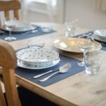 Holztisch mit blauen Platzsets und Geschirr für vier Personen.