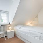 Schlafzimmer mit weißem Bett, Nachttisch und Stuhl unter Dachschrägen.