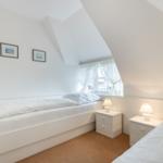Zimmer mit zwei Betten, Fenster und Nachttischen unter Dachschrägen.