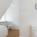 Zimmer mit zwei Betten, weißer Stuhl und Fenster unter Dachschräge.