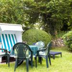 Garten mit Liegestuhl, Tisch und Stühlen. Grünflächen und Sträucher umgeben den Bereich.