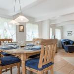 Esszimmer mit Holztisch und Stühlen, Wohnbereich mit blauen Sesseln und Fenstern mit weißen Vorhängen.