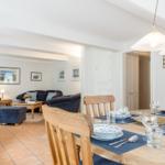 Esszimmer mit Holztisch und Stühlen, Wohnzimmer im Hintergrund mit Sofa und Fernseher.