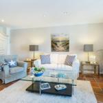 Wohnzimmer mit Sofa, zwei Sesseln, Glas-Tisch und Wandbild