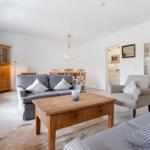 Wohnzimmer mit Sofa, Sessel und Holztisch. Küche und Essbereich im Hintergrund.