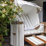 Strandkorb mit Streifenbezug und Kissen vor einem Haus mit Blumen