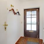 Eingangsbereich mit Holztür, Wandgarderobe und Sonnen-Spiegel.