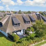 Haus mit Strohdach, Terrasse und Garten. Umgeben von Bäumen und Gras.