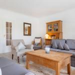 Wohnzimmer mit Sofa, Sessel und Holztisch. Bücherregal und Tür mit Glasfenstern.