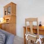 Holzschreibtisch mit Stuhl, Lampe und Telefon. Hintergrund: Holzschrank und Sofa mit Streifen.