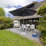 Terrasse mit Tisch, Stühlen und Sonnenschirm neben einem Haus mit Strohdach.